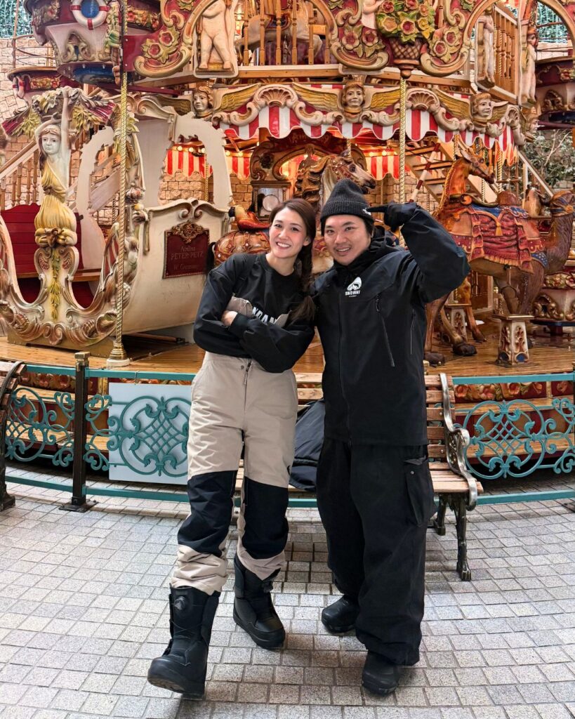 兩位穿著雪服的旅人在旋轉木馬前合照